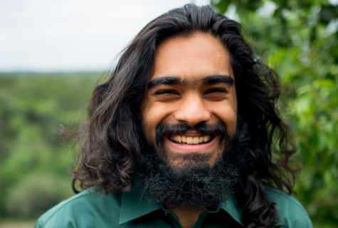 A portrait of Akash Thakkar standing outside and smiling widely with greenery in the background.